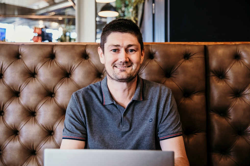 Mathew sitting in front of his laptop smiling at the camera.